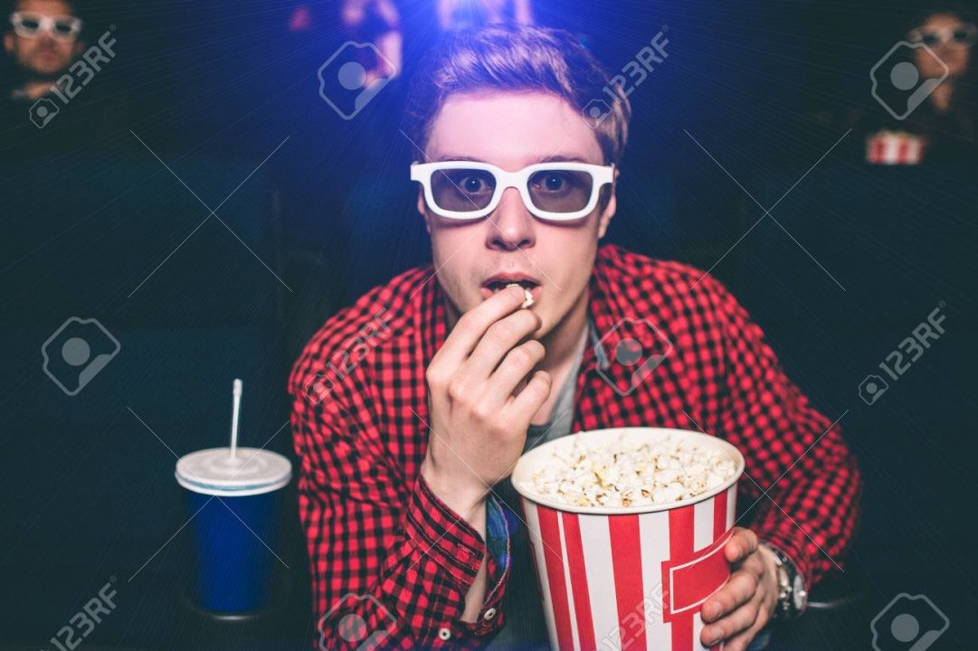 101349955-a-portrait-of-guy-sitting-in-chair-in-cinema-hall-and-eating-popcorn-he-is-looking-straight-very-int.jpg